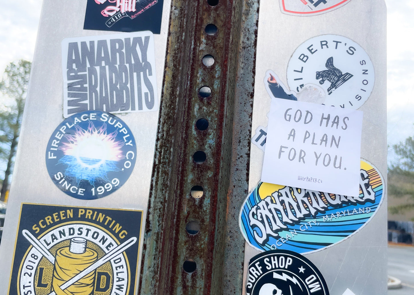Rust-covered metal surface with various stickers and a holypaperco tract on a cloudy day