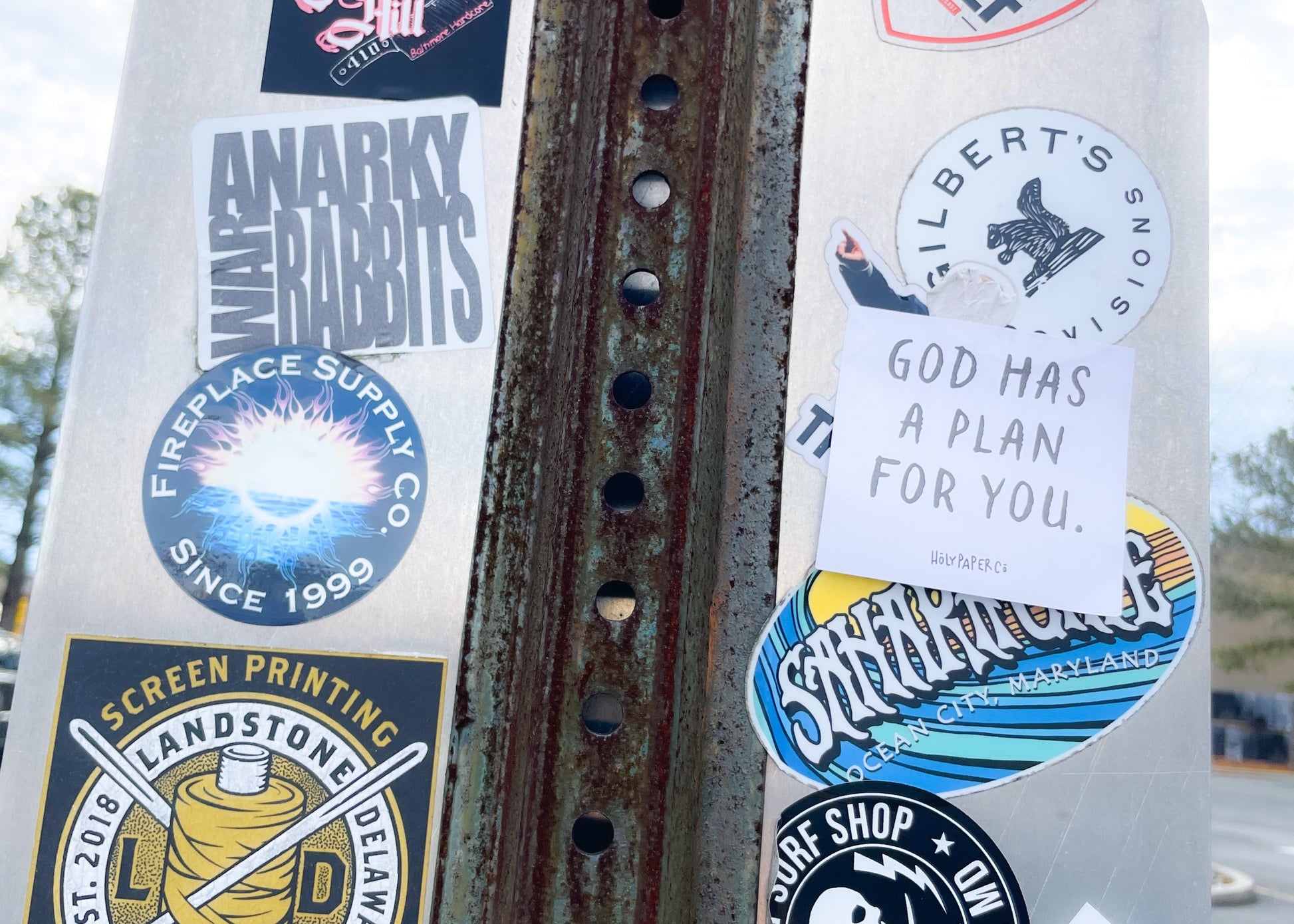 Rust-covered metal surface with various stickers and a holypaperco tract on a cloudy day