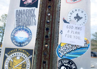 Rust-covered metal surface with various stickers and a holypaperco tract on a cloudy day